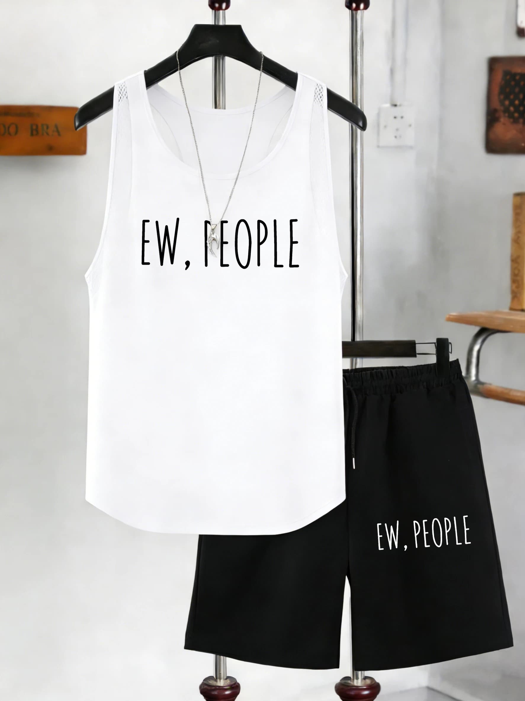 Completo da uomo con stampa artistica 'Ew People', composto da canotta in rete girocollo senza maniche e pantaloncini neri a gamba larga con tasche e coulisse, ideale per l'estate.