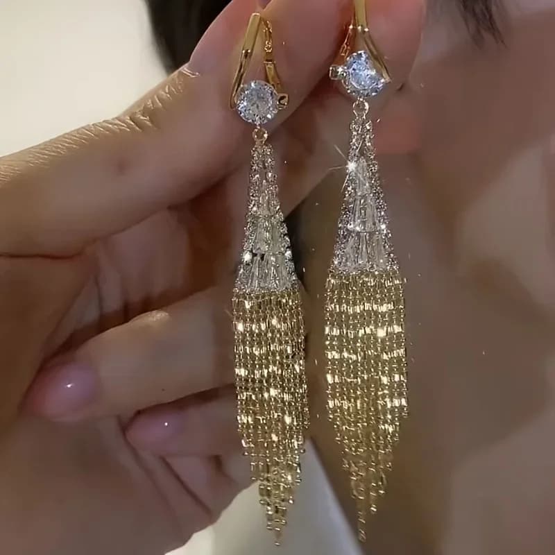 Il design presenta un circone cubico rotondo scintillante all'apice, seguito da una sezione affusolata tempestata di cristalli che si estende fino a una cascata di raffinate nappe a catena dorata.