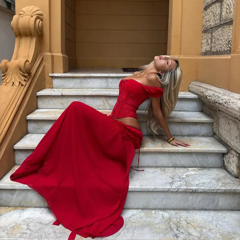Elegante completo rosso con top corsetto a spalle scoperte e gonna lunga a vita alta con volant e allacciatura posteriore, perfetto per le vacanze al mare.