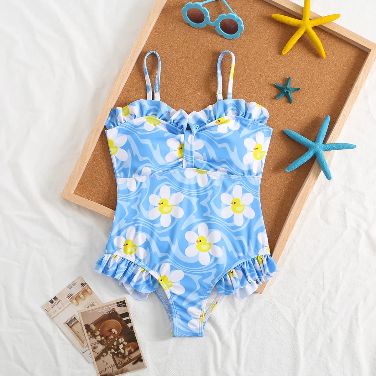 Full swimsuit for blue child with wave and daisies print, with thin shoulder straps, curled edge and V-neck, for the beach