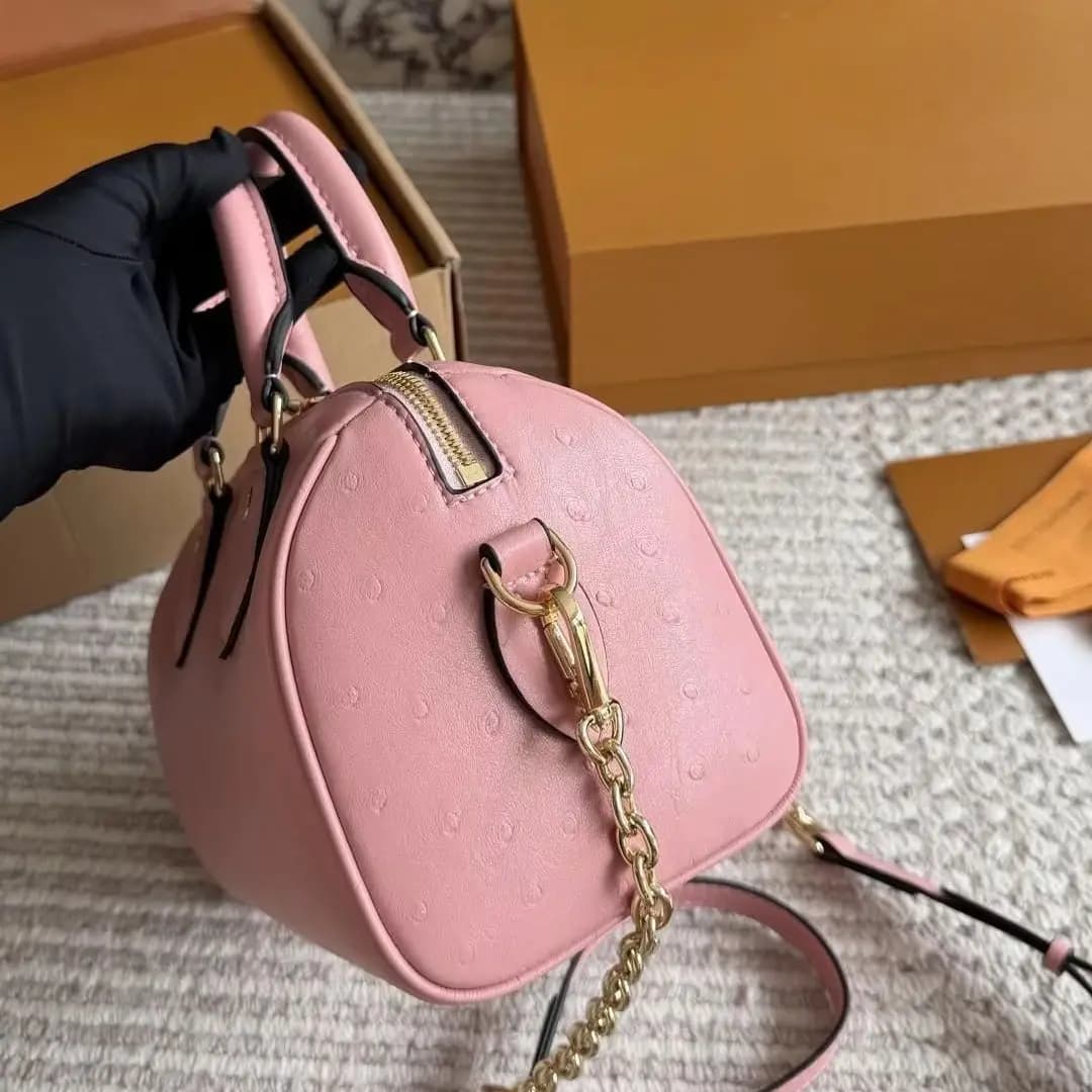 Pink Boston handbag with double top handles, gold lock and key hardware, removable chain crossbody strap, and zipper closure mini bucket bag for women.