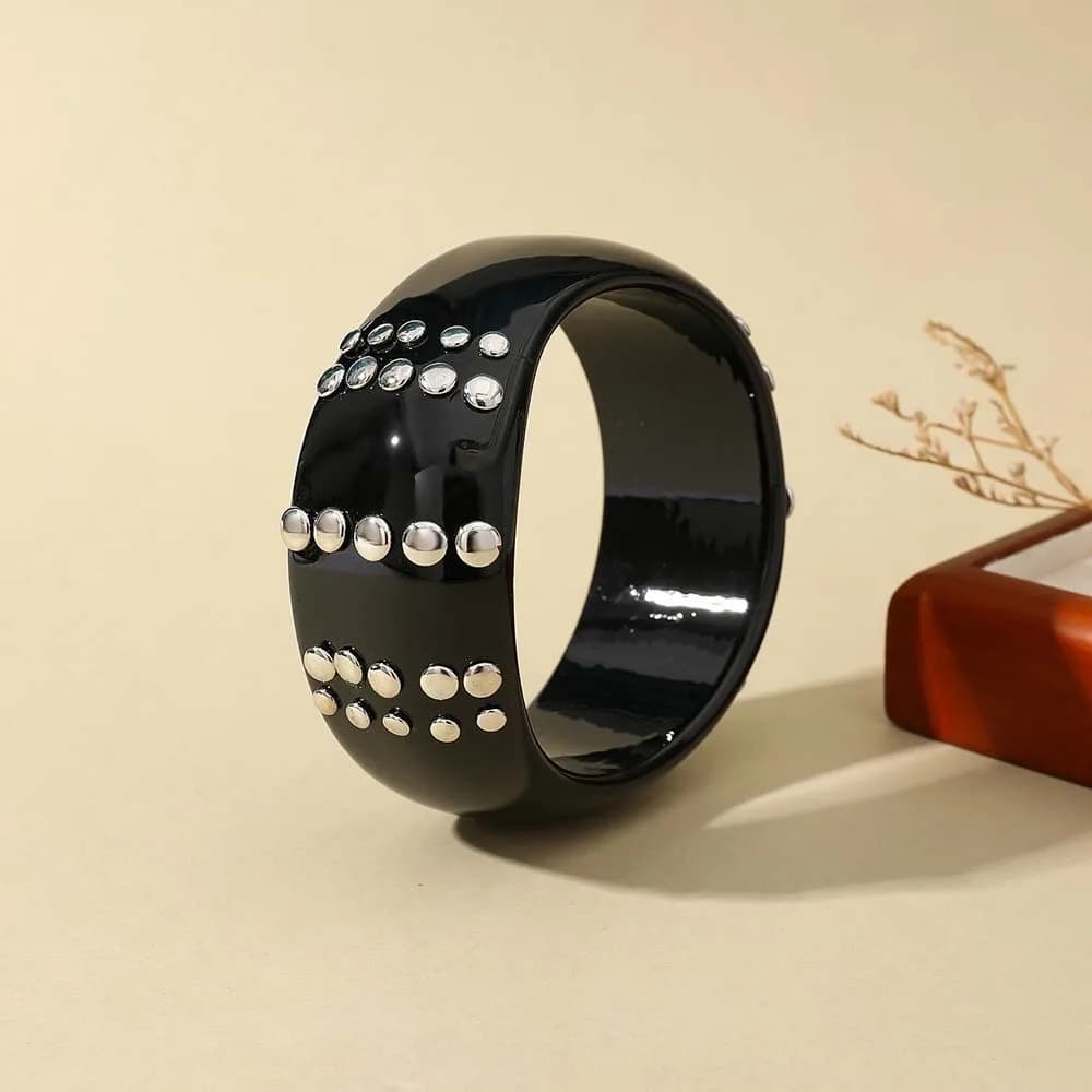Bracciale rigido in resina leggera con silhouette geometrica, borchie e finitura lucida, resistente