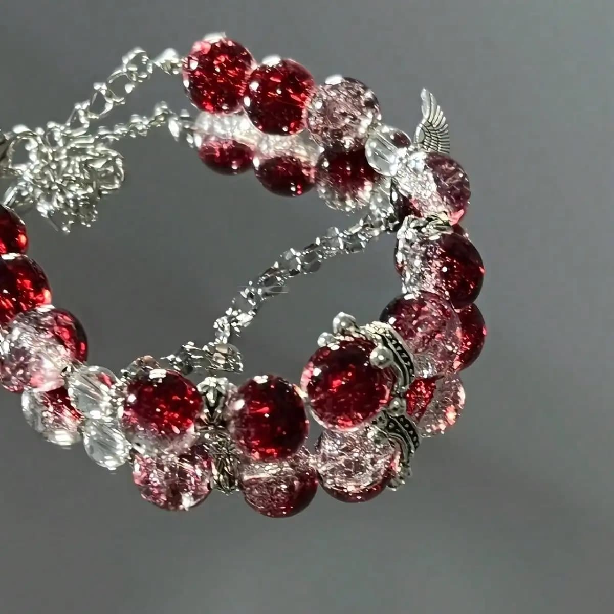 Bracciale con ciondolo in perline di cristallo rosso intenso e dettagli a forma di ali in argento