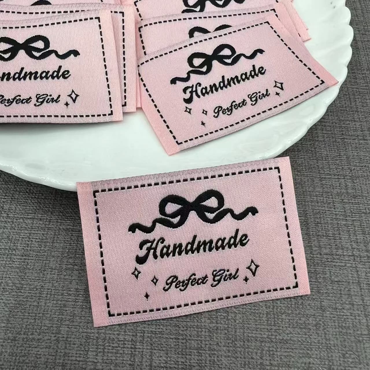 Etichette tessute fatte a mano personalizzate | Etichette in tessuto arrotolato e design con papillon | Etichette pieghevoli per la cura del cotone per abbigliamento (disponibili)